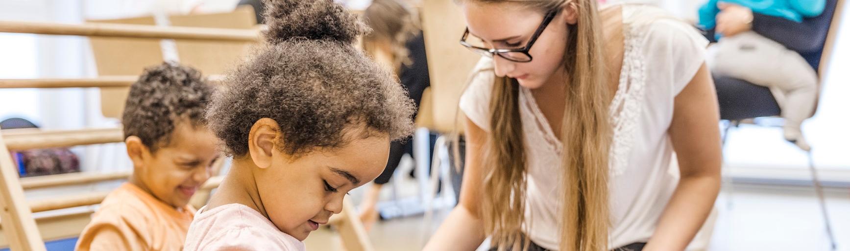 Eltern und KInder im Eltern-Kind-Kurs, im Vordergrund eine Mutter mit Kindern beim Spiel