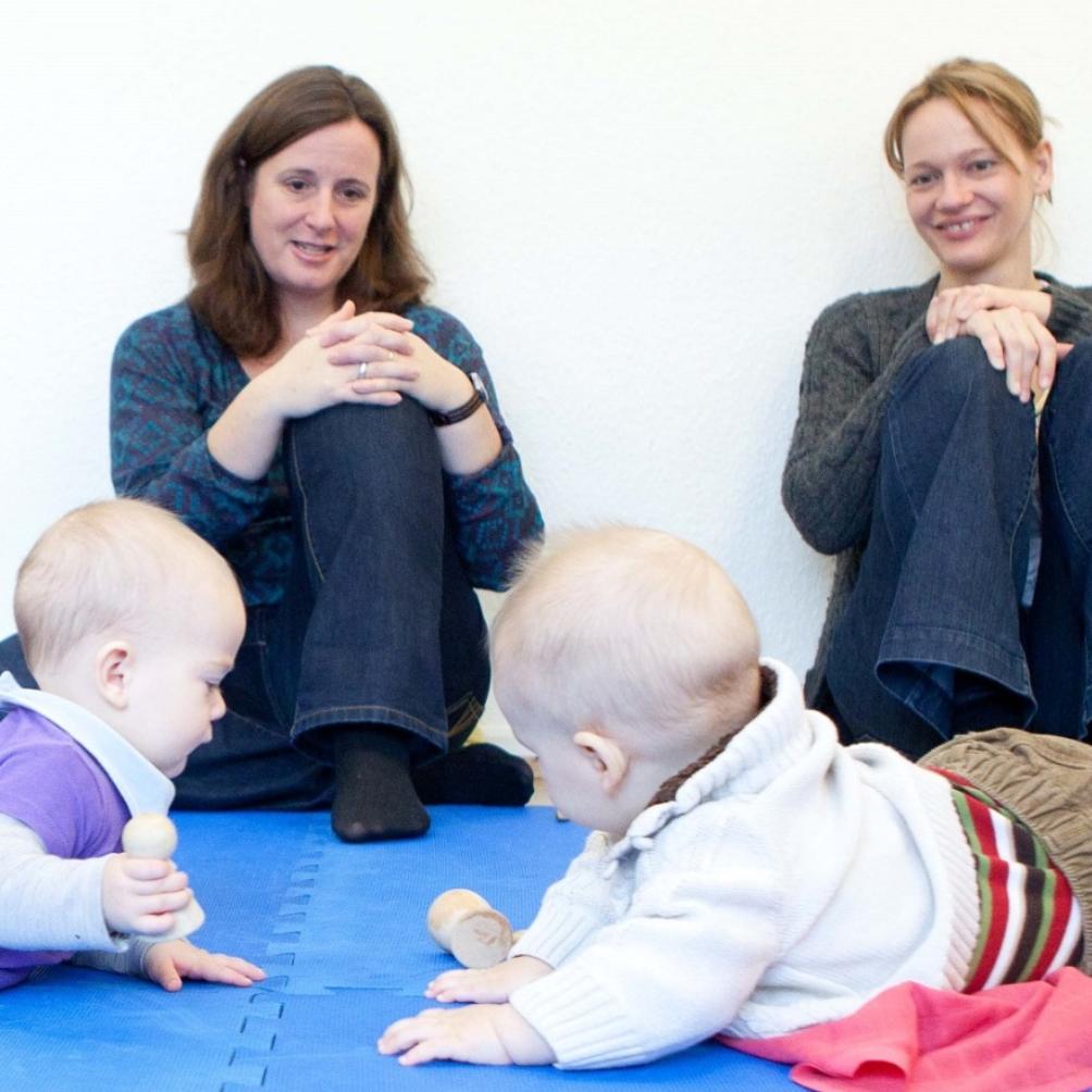 Väter und Mütter sehen Kindern beim Spiel im Eltern-Kind-Kurs zu.