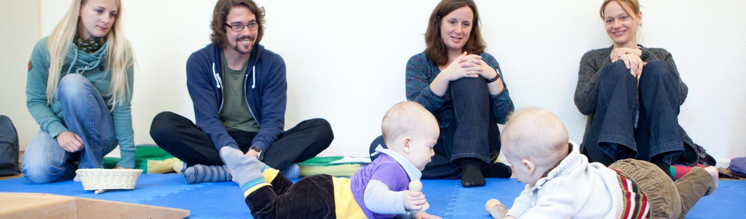 Väter und Mütter sehen Kindern beim Spiel im Eltern-Kind-Kurs zu.