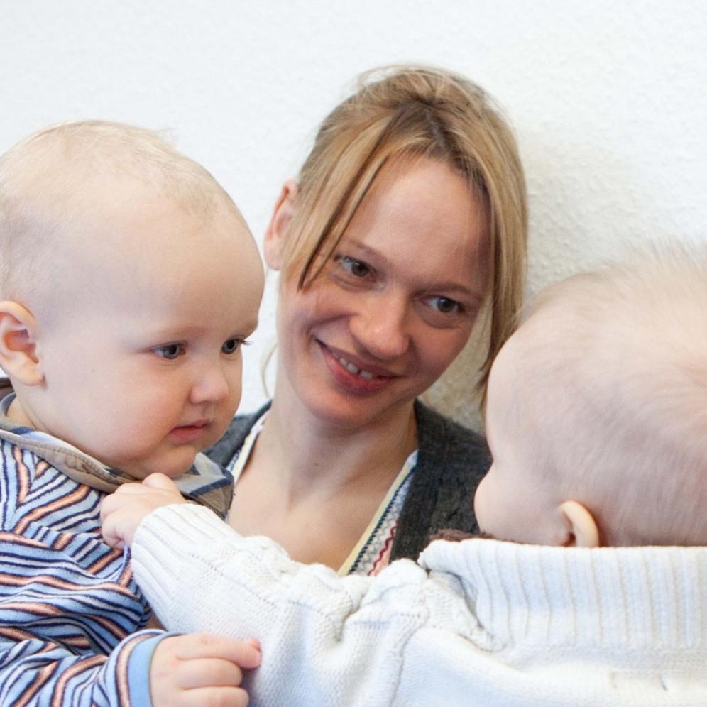 Zwei Mütter mit ihren Babies auf dem Schoß schauen interessiert zu, wie ihre Babies im Eltern-Kinder-Kurs aufeinander reagieren.