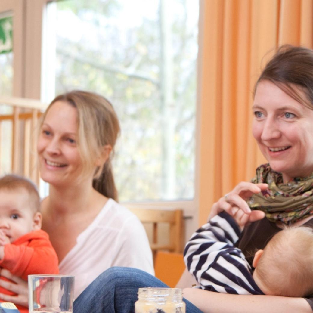 Väter und Mütter mit ihren Kindern auf dem Schoß hören im Eltern-Kind-Kurs aufmerksam zu.