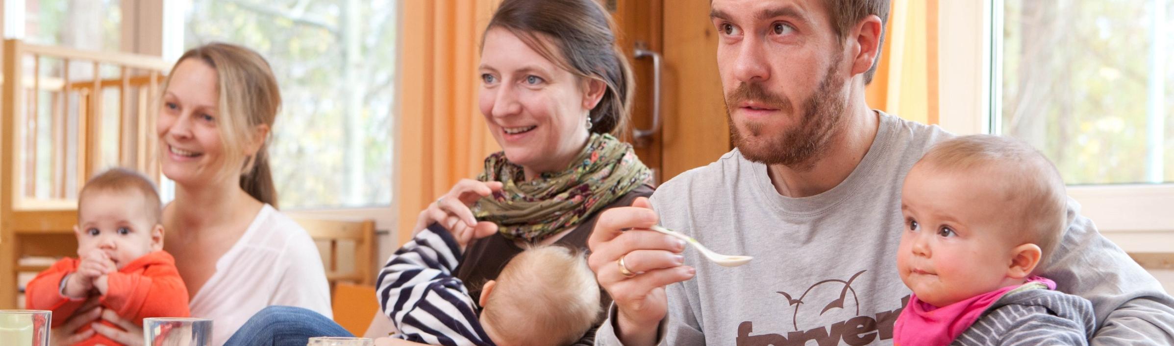 Väter und Mütter mit ihren Kindern auf dem Schoß hören im Eltern-Kind-Kurs aufmerksam zu.