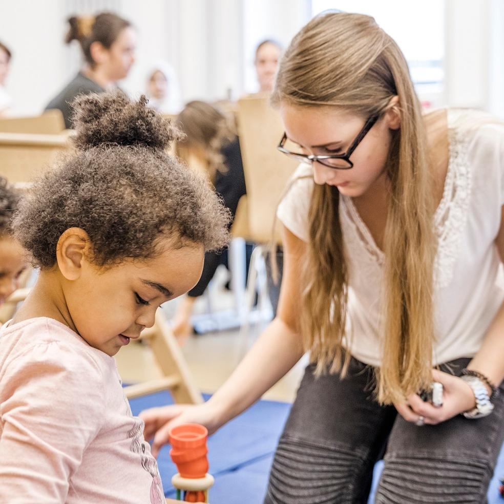 Eltern und KInder im Eltern-Kind-Kurs, im Vordergrund eine Mutter mit Kindern beim Spiel
