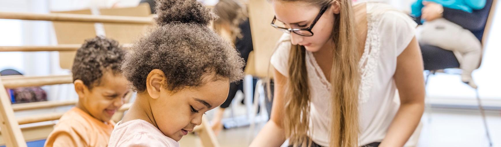 Eltern und KInder im Eltern-Kind-Kurs, im Vordergrund eine Mutter mit Kindern beim Spiel