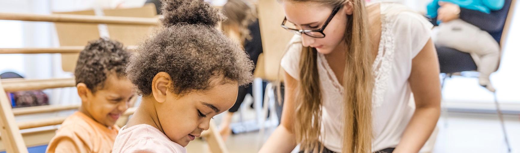 Eltern und KInder im Eltern-Kind-Kurs, im Vordergrund eine Mutter mit Kindern beim Spiel