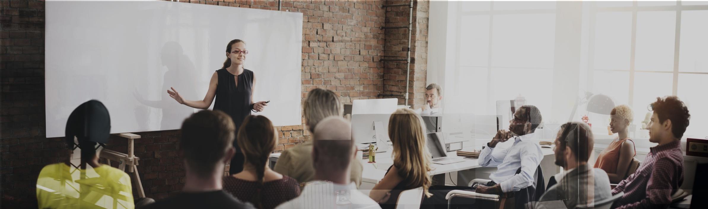 Erwachsenenbildung - Kursleiterin referiert vor einem Smartboard, die Kursgruppe hört aufmerksam zu