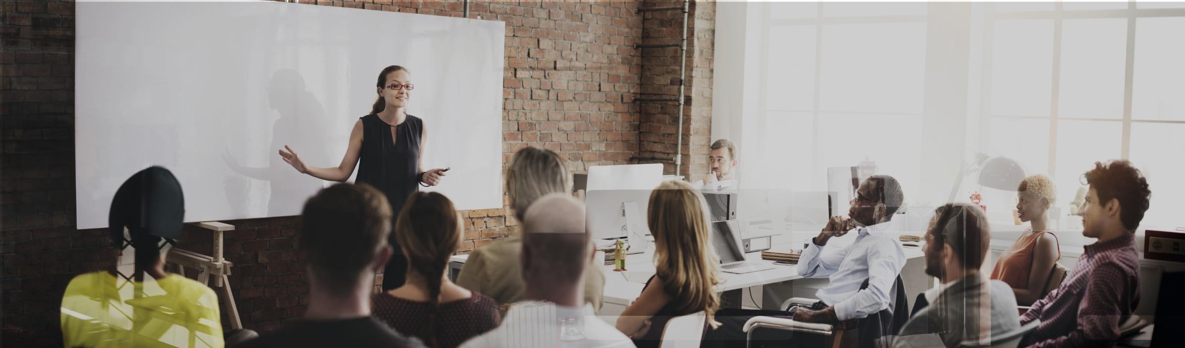 Erwachsenenbildung - Kursleiterin referiert vor einem Smartboard, die Kursgruppe hört aufmerksam zu