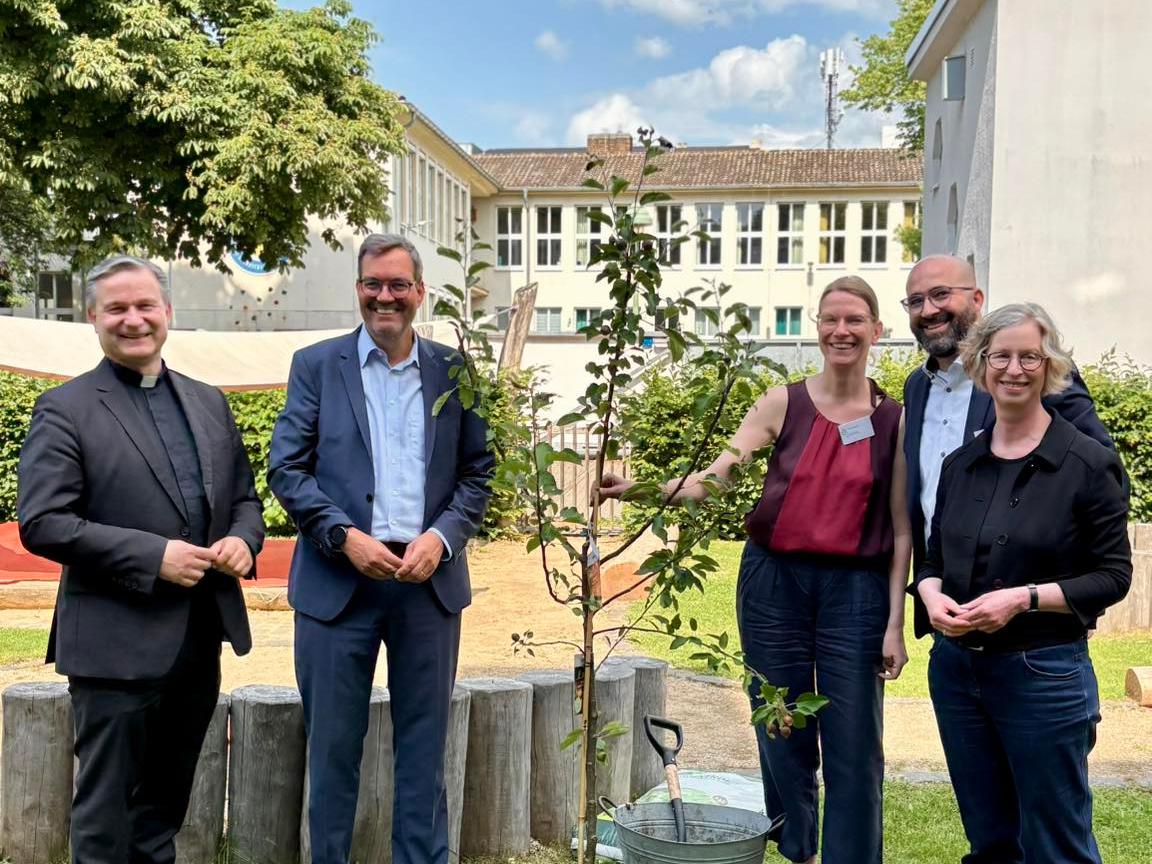 Msgr. Markus Hofmann, Bürgermeisterin Nicole Unterseh, Stefan von der Bank (pädagogischer Leiter des Bildungswerks der Erzdiözese Köln e.V.), Manuel Hetzinger (Leiter Katholisches Bildungsforum Bonn) und Doris Bremm (stellvertretende Leiterin Katholisches Bildungsforum Bonn) pflanzen einen Apfelbaum im Garten der Katholischen Familienbildungsstätte Bonn