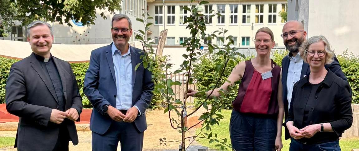 Msgr. Markus Hofmann, Bürgermeisterin Nicole Unterseh, Stefan von der Bank (pädagogischer Leiter des Bildungswerks der Erzdiözese Köln e.V.), Manuel Hetzinger (Leiter Katholisches Bildungsforum Bonn) und Doris Bremm (stellvertretende Leiterin Katholisches Bildungsforum Bonn) pflanzen einen Apfelbaum im Garten der Katholischen Familienbildungsstätte Bonn