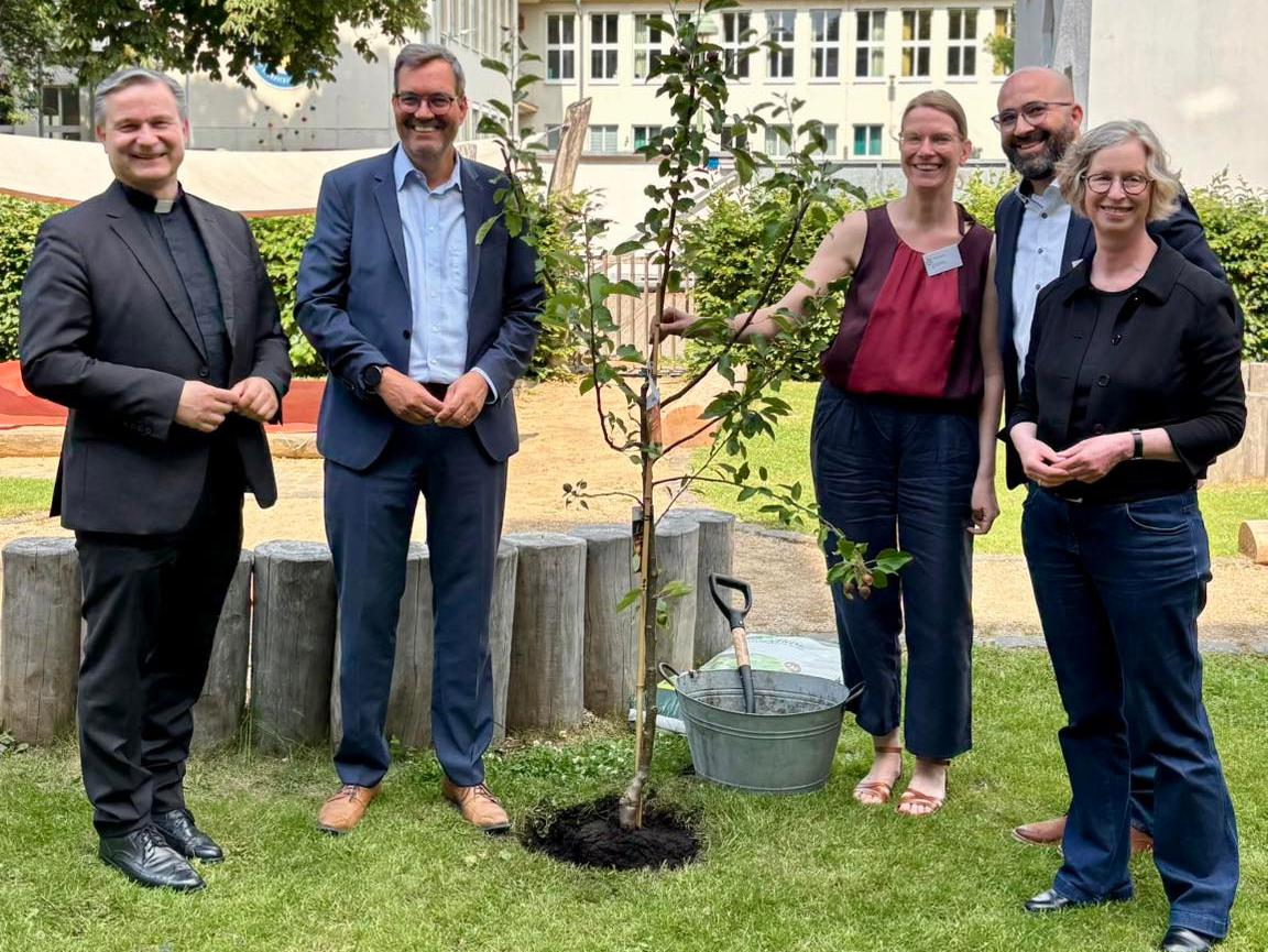 Msgr. Markus Hofmann, Bürgermeisterin Nicole Unterseh, Stefan von der Bank (pädagogischer Leiter des Bildungswerks der Erzdiözese Köln e.V.), Manuel Hetzinger (Leiter Katholisches Bildungsforum Bonn) und Doris Bremm (stellvertretende Leiterin Katholisches Bildungsforum Bonn) pflanzen einen Apfelbaum im Garten der Katholischen Familienbildungsstätte Bonn