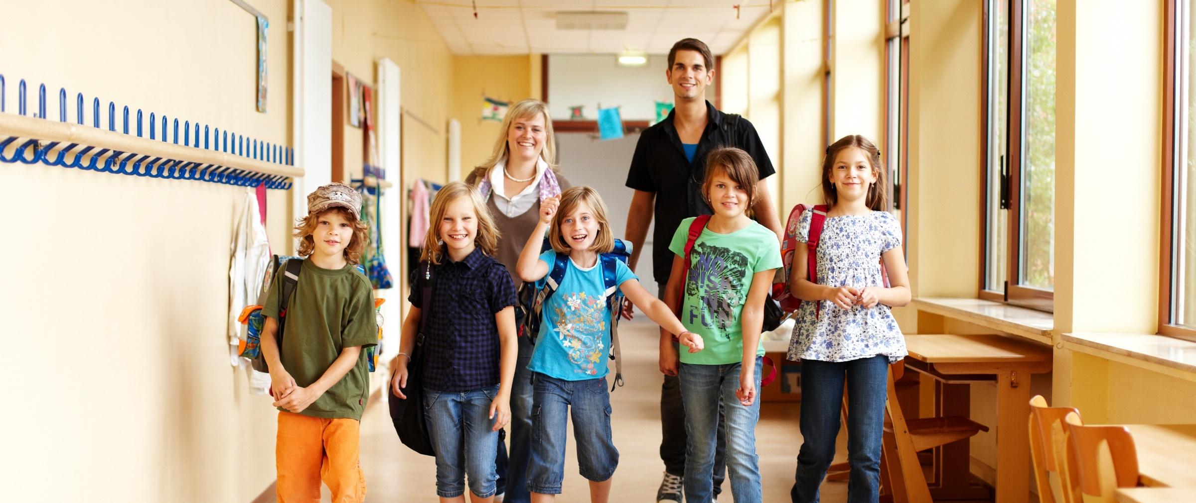 Fünf Schulkinder mit einem Betreuer und einer Betreuerin auf einem Schulflur