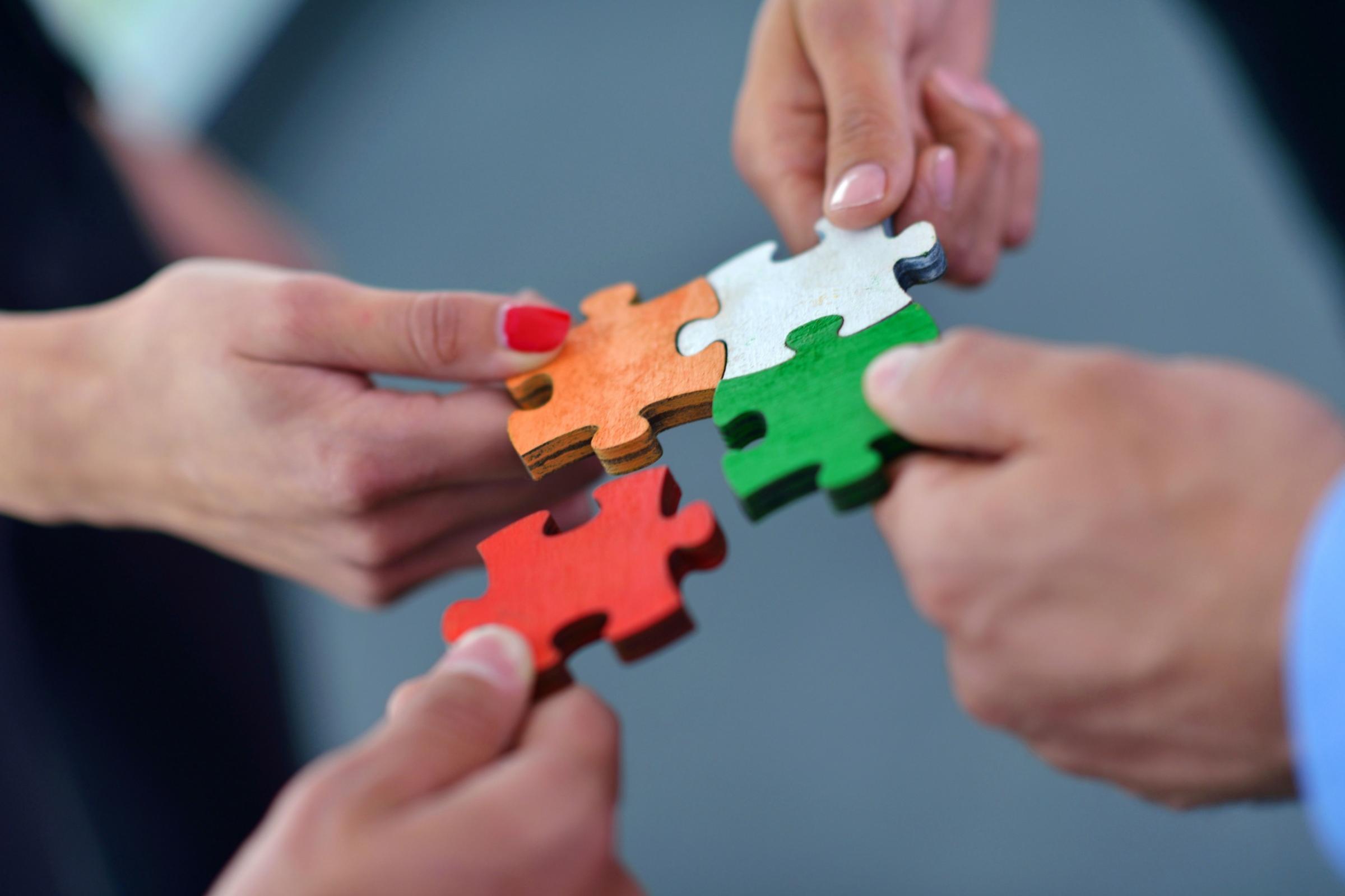 Hände setzen bunte Puzzleteile zusammen.