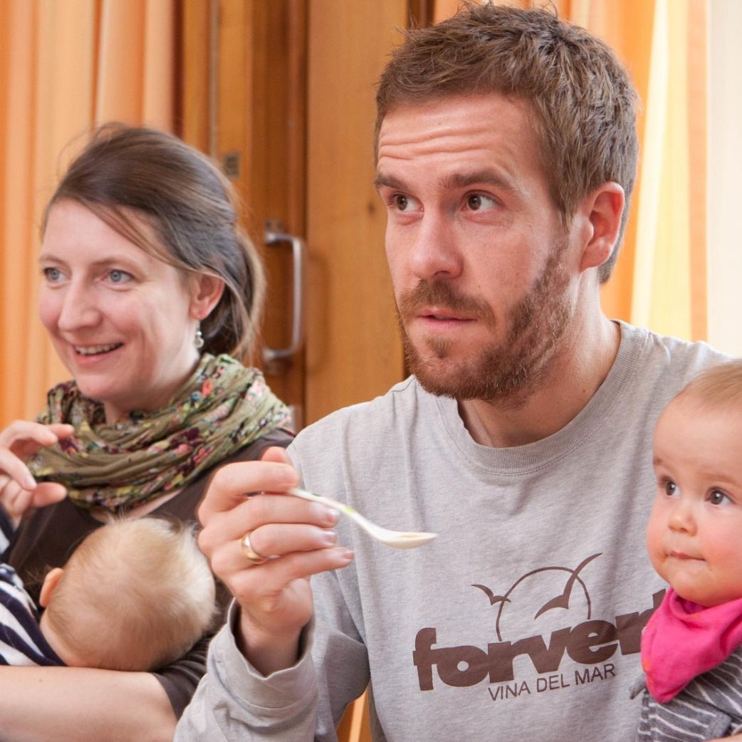 Väter und Mütter mit ihren Kindern auf dem Schoß hören im Eltern-Kind-Kurs aufmerksam zu.