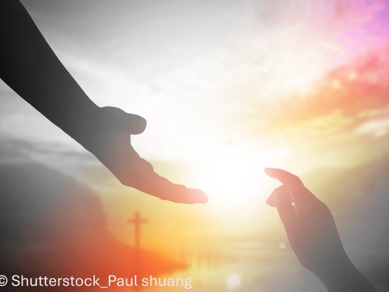 Ausgestreckte Hände vor Kreuz und rotem Himmel
