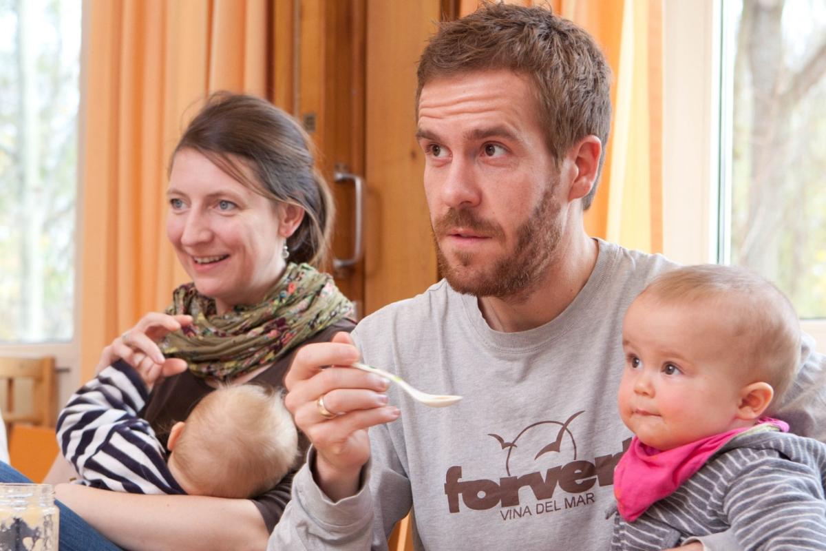 Väter und Mütter mit ihren Kindern auf dem Schoß hören im Eltern-Kind-Kurs aufmerksam zu.